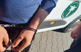 Mężczyzna z założonymi kajdankami na rękach stoi przed samochodem służbowym Inspekcji Transportu Drogowego.